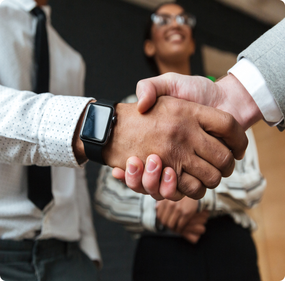 Two people shaking hands in an office while a colleague looks on.