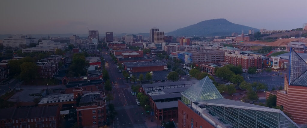 Aerial view of downtown Chattanooga at dusk, with the Tennessee Aquarium and Lookout Mountain beyond.