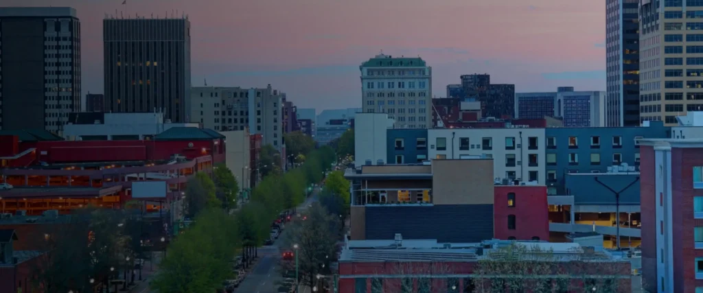 Downtown Chattanooga's skyline at dusk, with a tree-lined street below a pink sky.